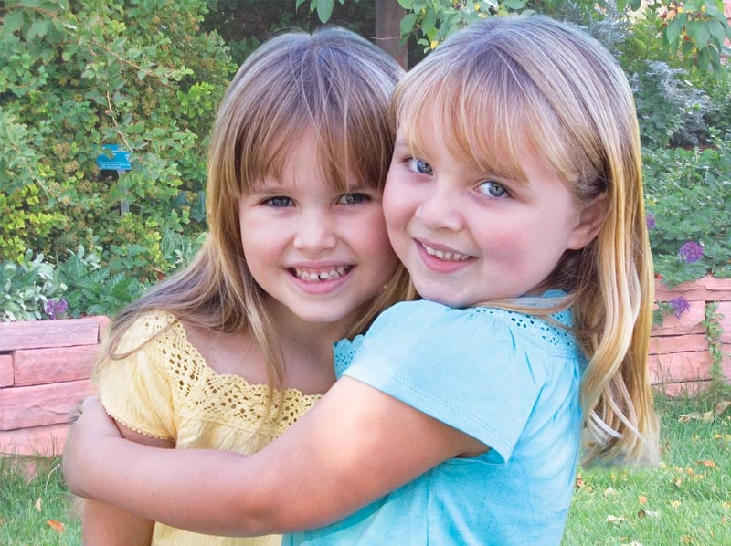 Two young girls smiling and hugging.
